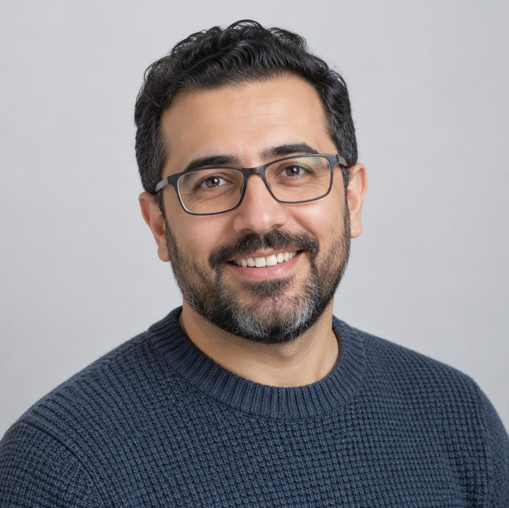 Studio portrait of a smiling man with glasses and a beard wearing a sweater